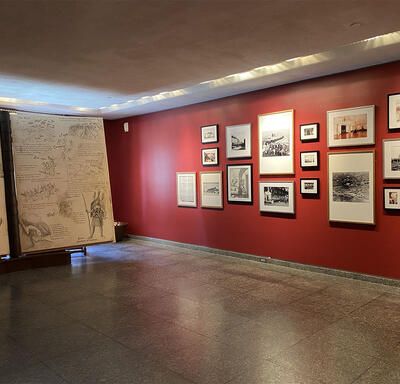 There is a large 2-piece display of sketches and text on the left. A red wall featuring a mix of 17 photographs, sketches and paintings is on the right.