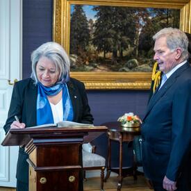 Governor General Simon signing a guest book. President Sauli Niinistö is standing to her right.